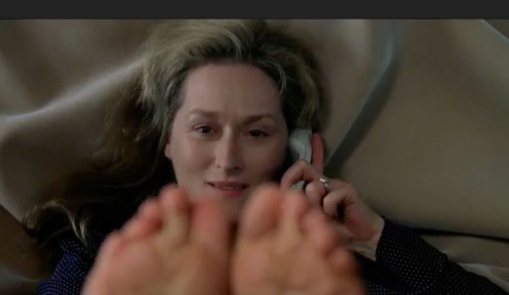 screenshot of Meryl Streep in adaptation, playing Susan Orlean, who is high and on the phone trying to get her conversation partner to hum in the right harmonics to make a dial tone. she is lying on a buff blanket staring at her toes, which are up in the air