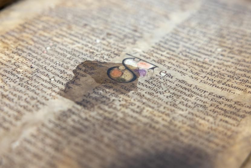 Old manuscript covered in lines of medieval Irish script written in black ink, with an decorative S in the centre