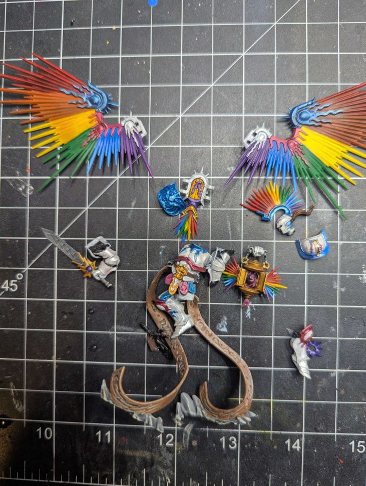 A disassembled miniatures from Age of Sigmar painted in Pride colors: white armor with pink and blue accents, and rainbow wings