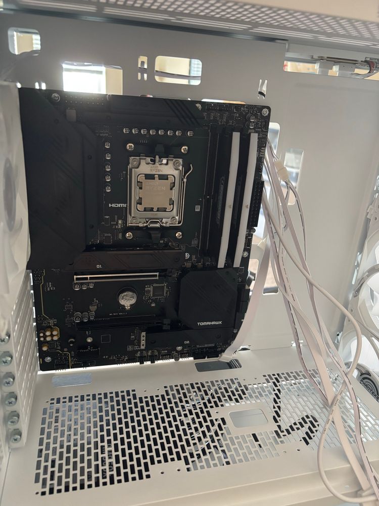 A picture of the open front of a PC case, with the black motherboard mounted along with RAM and the processor. There's no graphics card mounted or heatsink on the processor, nor is anything plugged in. White cables hang out of the front of the care.