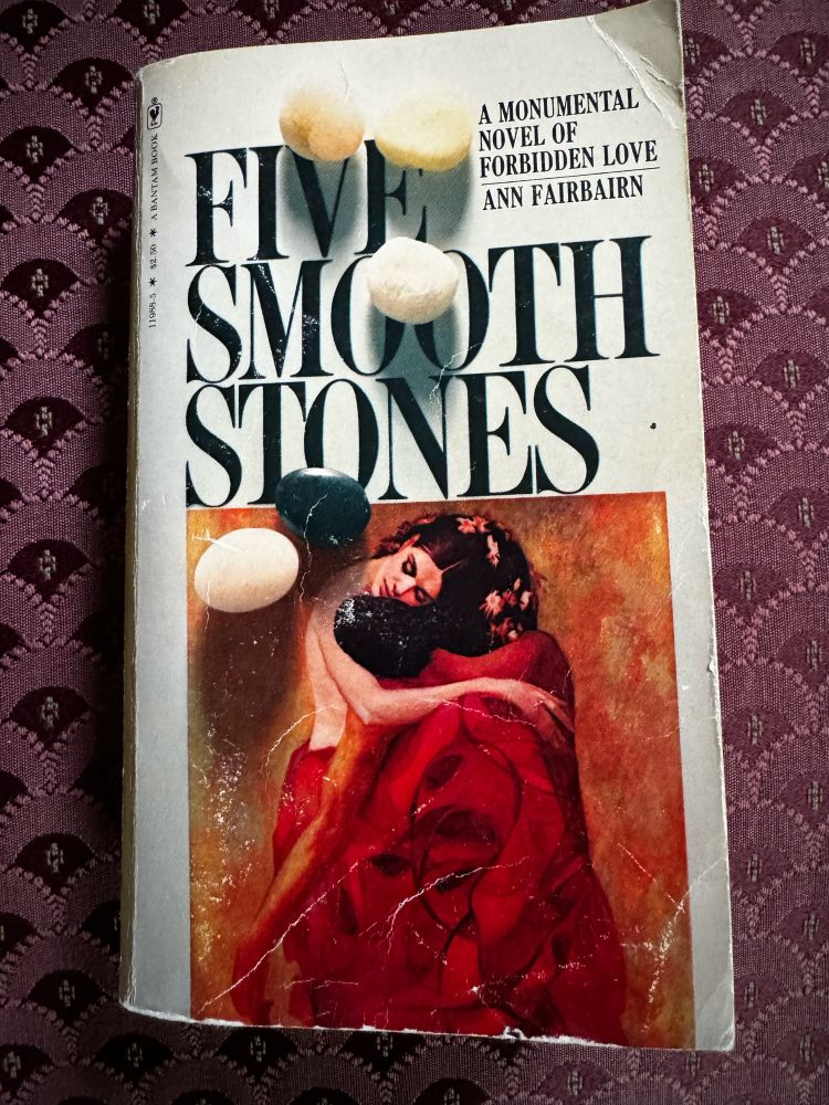 Cover of the book Five Smooth Stones by Ann Fairbairn showing a couple embracing. fFour white stones and one black stone are laid over the cover. 