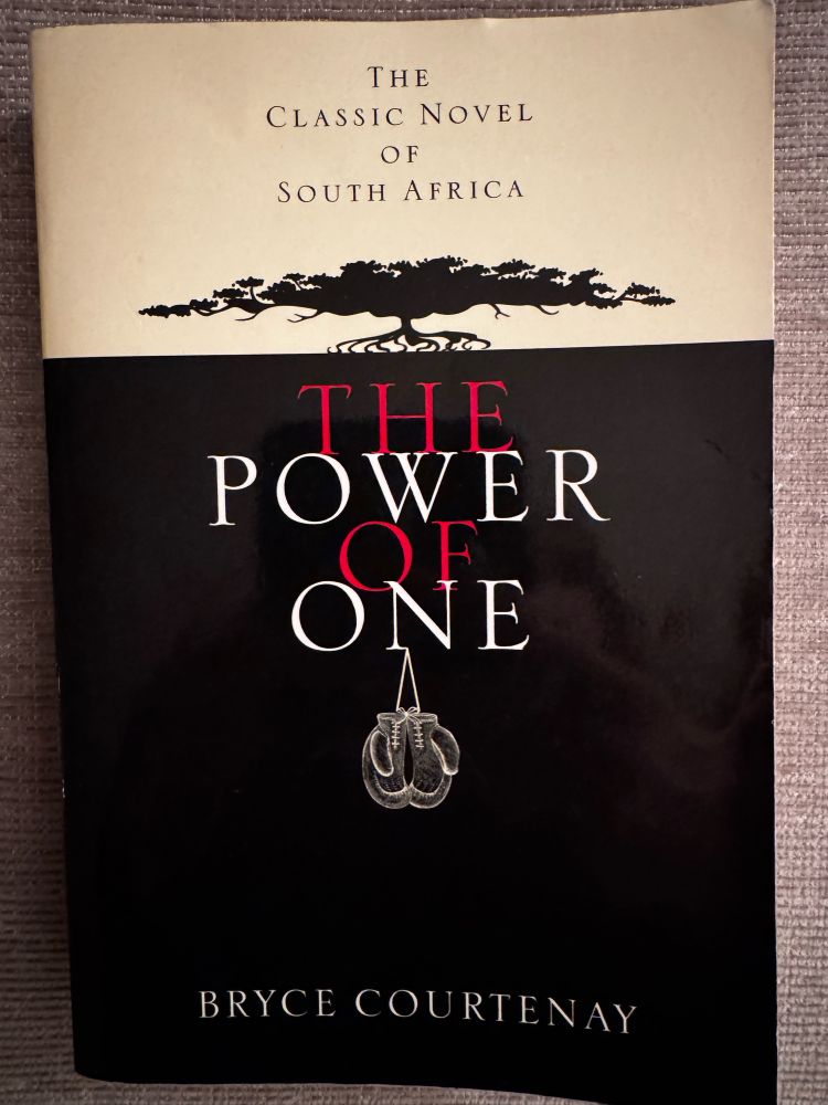 The cover of the book The Power of One by Bryce Courtenay, showing a black tree with boxing gloves hanging from the title. 