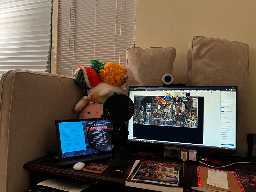 A desk with a microphone and couch cushions + child’s stuffed animals set around it to absorb sound and improve recording quality.