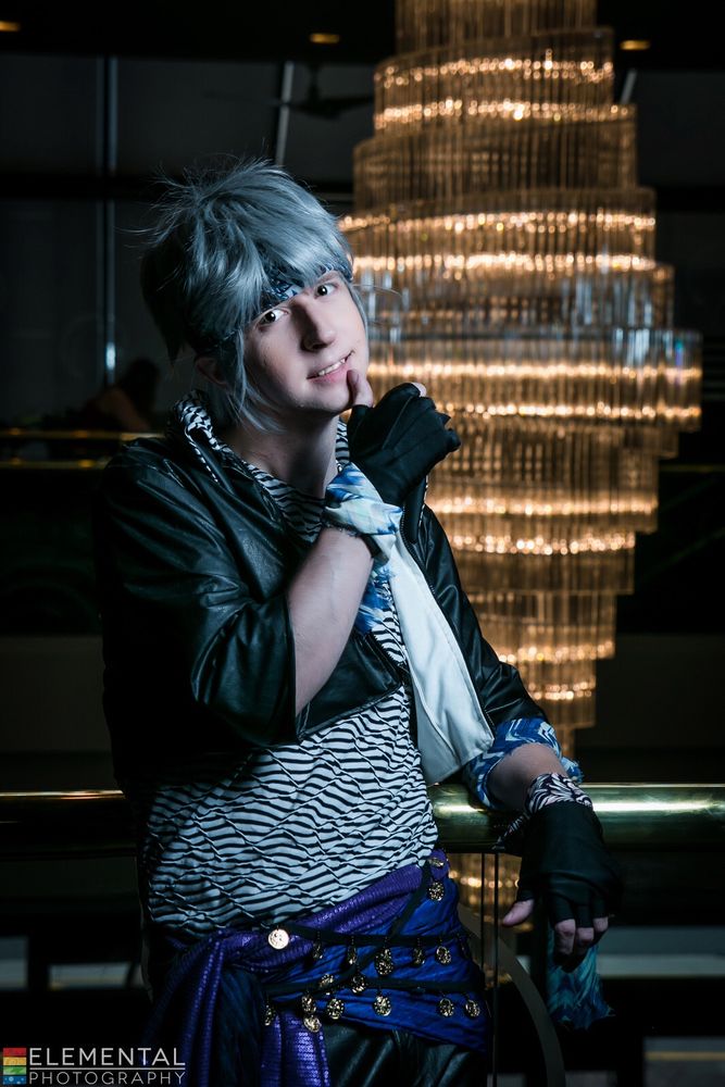 Locke Cole cosplayer, wearing black leather pants, cropped leather jacket, stripped shirt, purple and blue sash and fingerless gloves. 