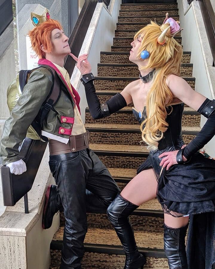 The previous image taken from a different angle, showing their full bodies. The prince has a turtle shell on his back and black leather pants. The Bowsette is wearing long black gloves, a black corseted dress and thigh high boots. 