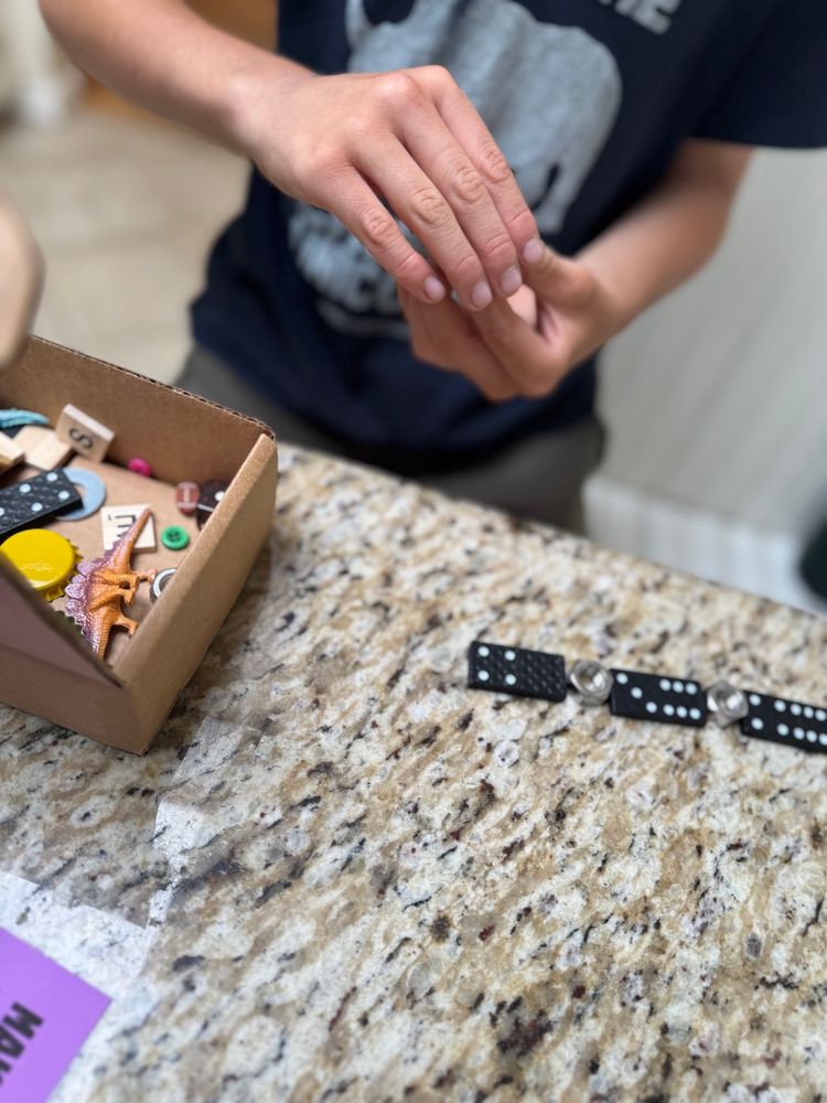 Dominos and silver Lugnuts in pattern. On corner of photo there’s a small cardboard box full of small trinkets. 