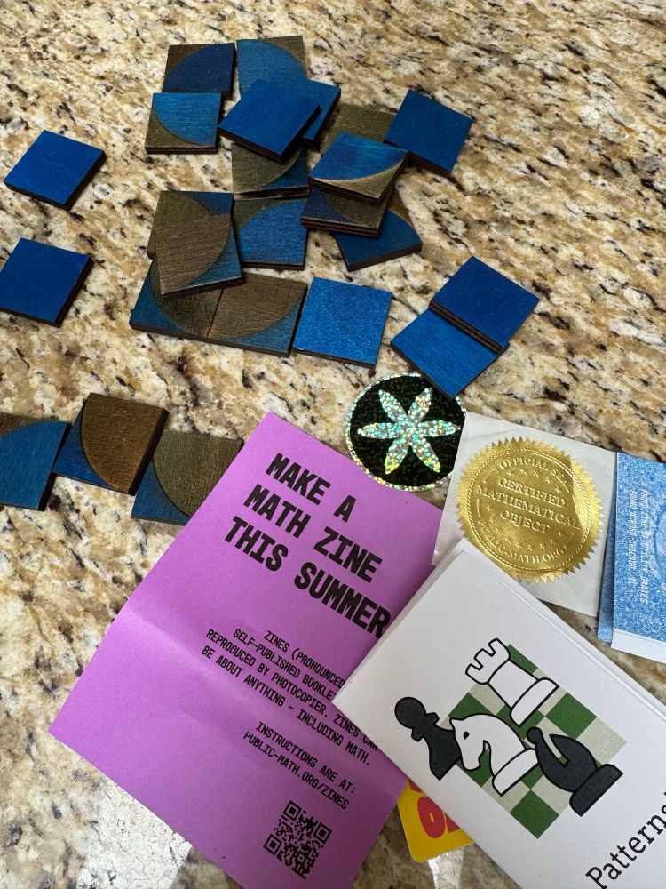 Swirly blue and black trucker tiles, sparkling sticker with a six pointed flower design, purple paper with “make a zine this summer”, small white paper zine with chess pieces and “patterns” on front. Gold sticker. 