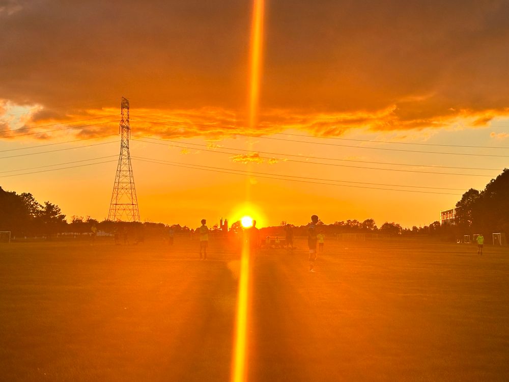 Soccer being played, maybe.  Hard to tell with the sun in everyone’s eyes. Some shadows of players are seen.