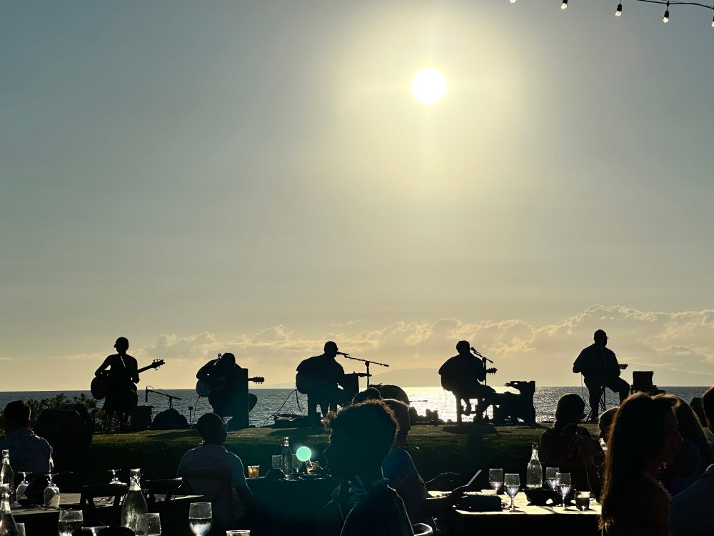 The silhouette of a five piece band in front of a blazing sun.  