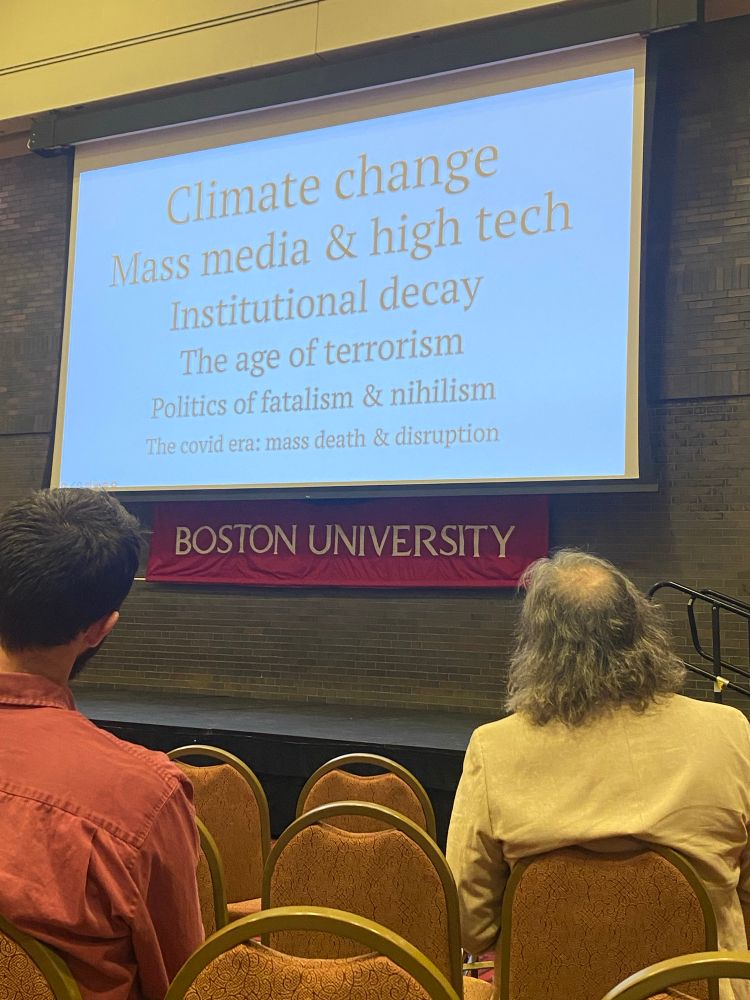 Power point slide that says “climate change, mass media and high tech, institutional decay, the age of terrorism, politics of fatalism and nihilism, The Covid era: mass death and destruction