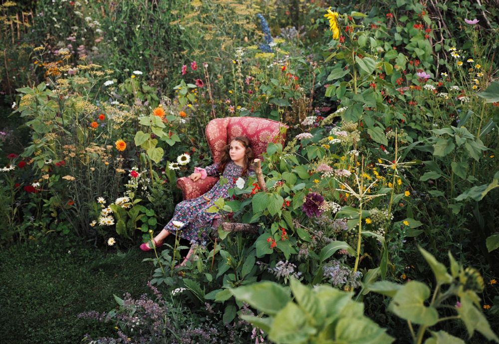 une jeune fille assise dans un fauteuil rose au coeur d’un jardin extraordinaire en fleurs
