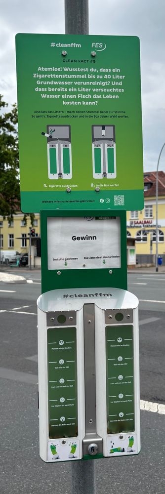 Sogenannter Meinungsfilter … eine Zigarettenkippenentsorgungsstation an einem Masten. Auf einem Schild wird erklärt, wie schädlich eine einzelne Kippe für das Grundwasser ist. Die eigene Kippe kann man in einen Entsorgungsbehälter werfen und sich für Glück beim Spiel oder der Liebe entscheiden.