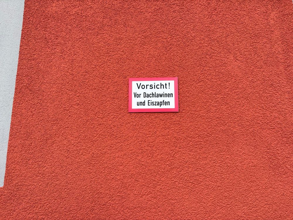 An einer Hauswand angebrachte Tafel mit der Aufschrift ‚Vorsicht! Vor Dachlawinen und Eiszapfen