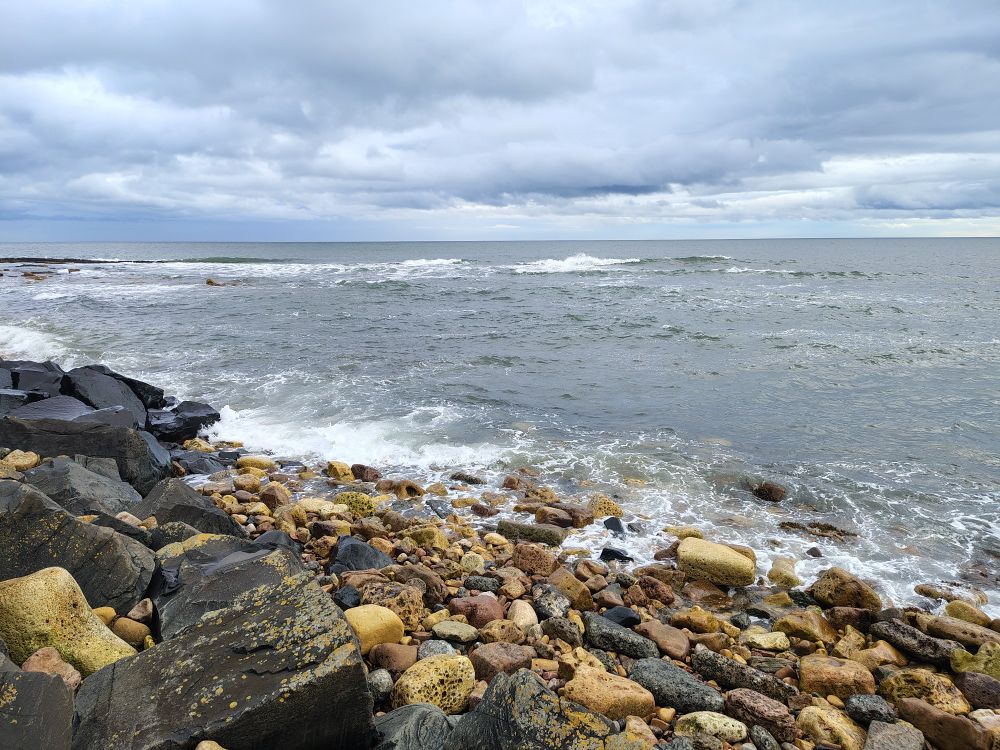 Rocky shoreline with the sea and gray clouds. 