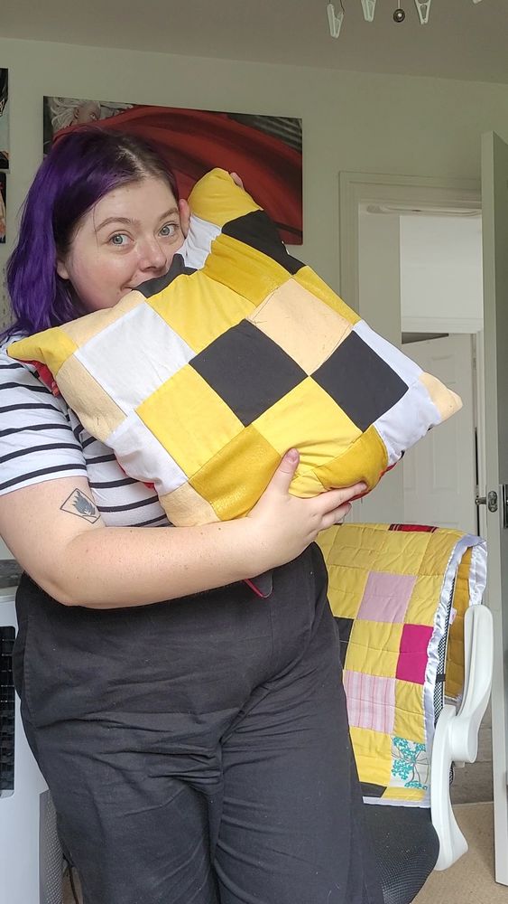 Holly holding the scrap cushion she made, which consists of yellow patterns.