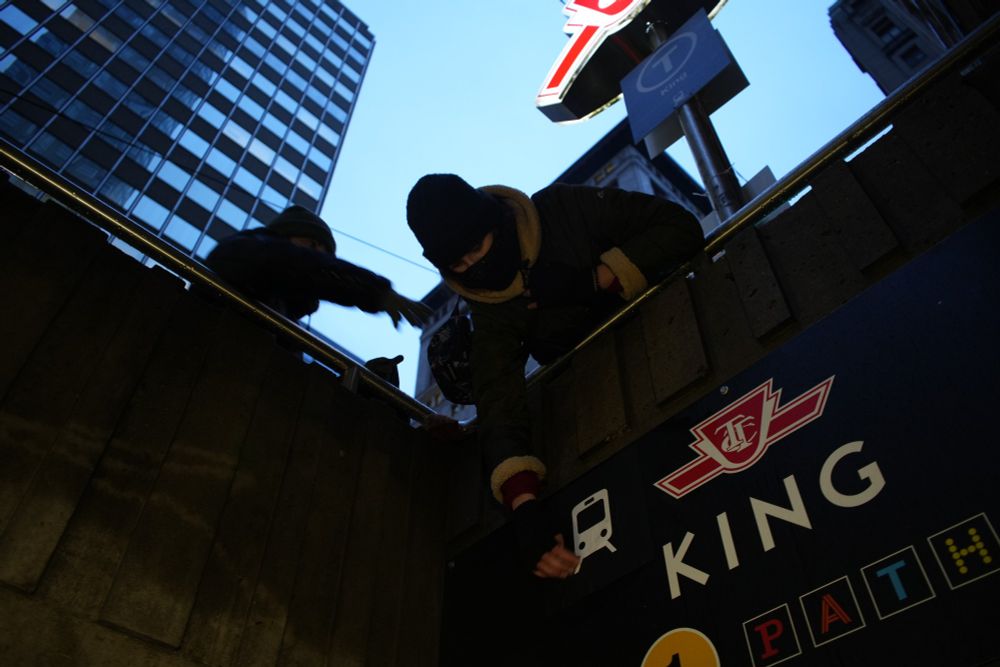 two volunteers leaning over subway entrance pasting signs