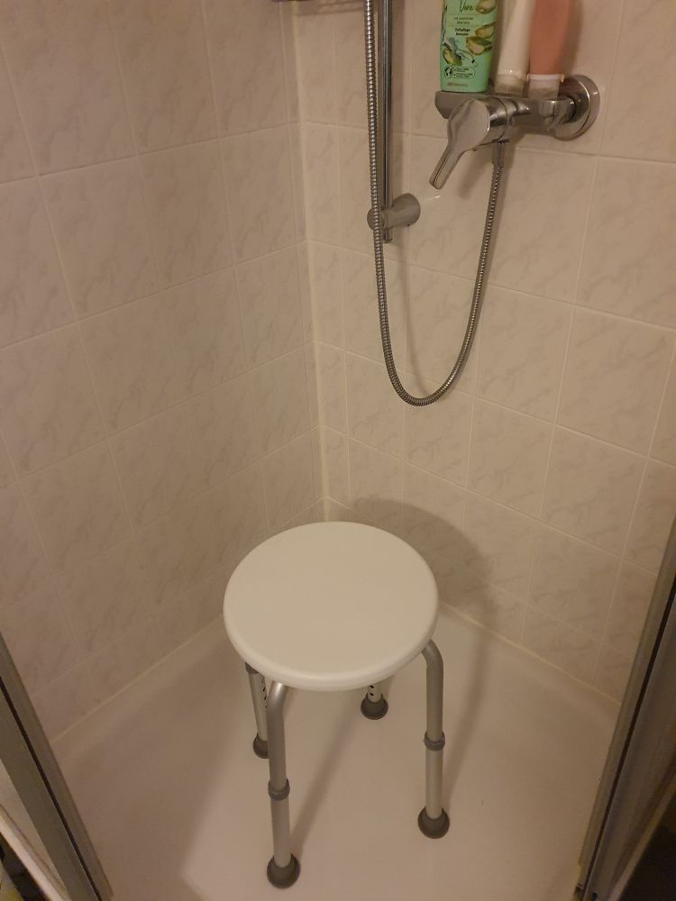 Ein kleiner Duschhocker in einer sehr kleinen Dusche.