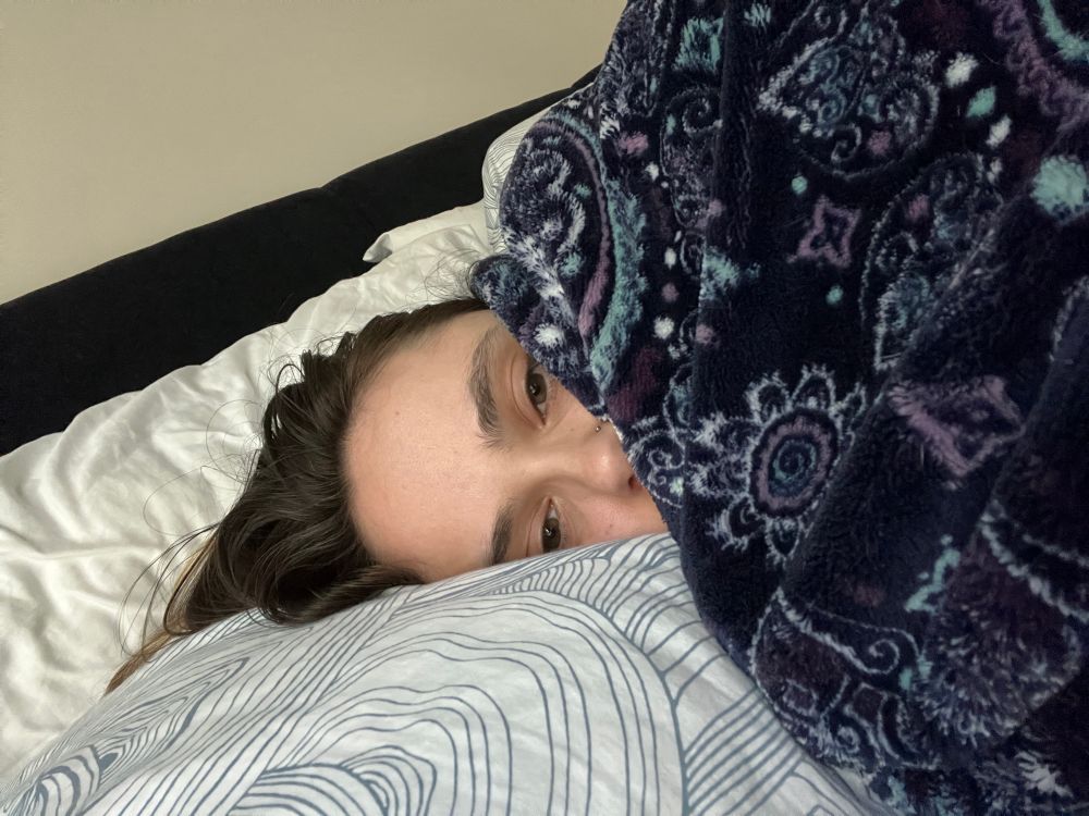 Bunny in bed wrapped up in a soft blue blanket covering half their face.