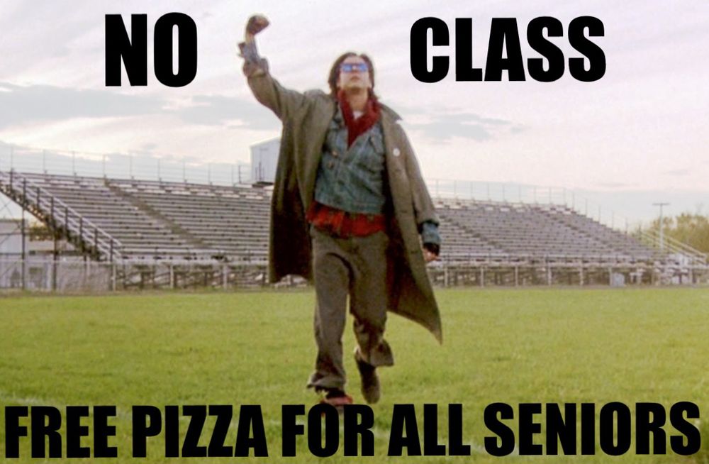 A still image from the movie, the breakfast club showing Judd Nelson’s character walking across a football field with bleachers in the background. He is wearing shabby punk rock clothes and is pumping his right fist in the air in a gesture of triumph.