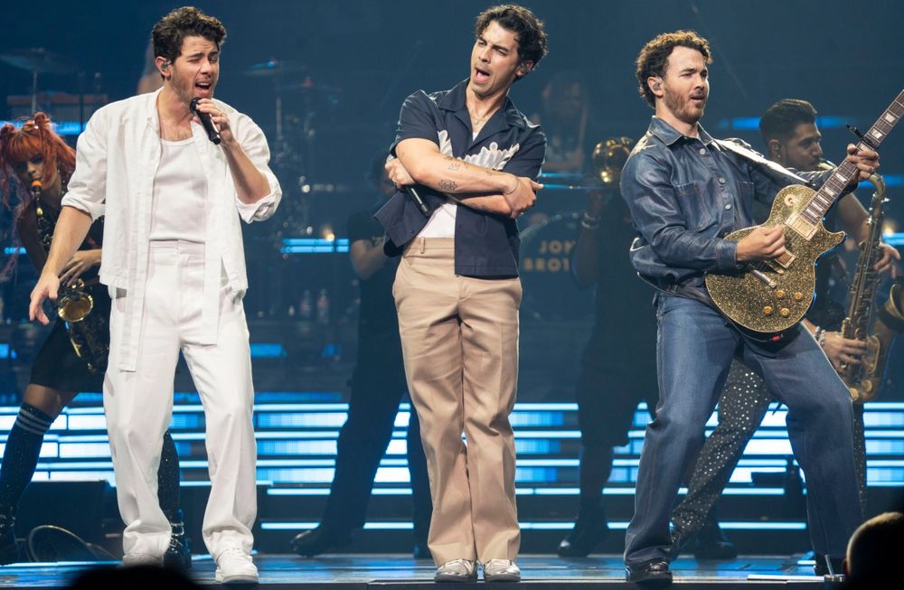 Jonas Brothers in concert. Nick in white, Kevin in full jean and Joe wearing a baseball shirt.
