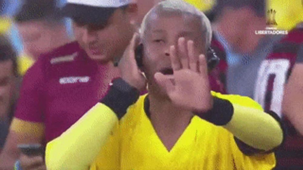 a man in a yellow shirt is covering his mouth with his hands