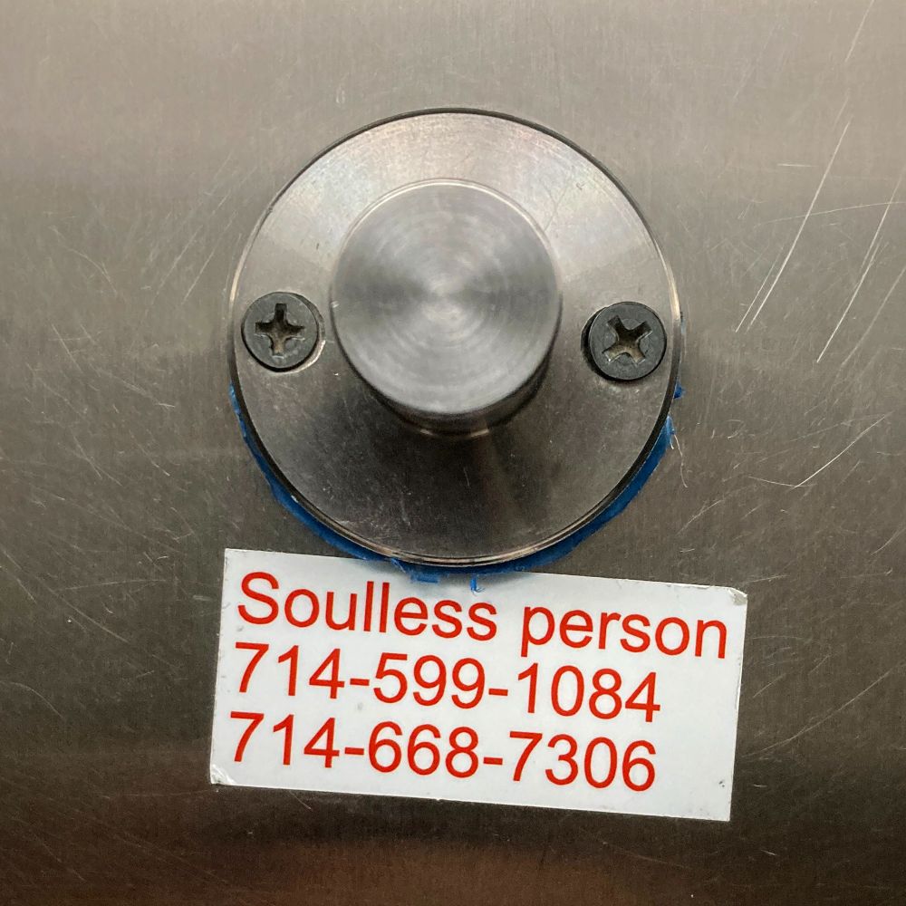 A coat hook on a bathroom stall door, with a sticker below it saying "Soulless person" and providing two phone numbers.