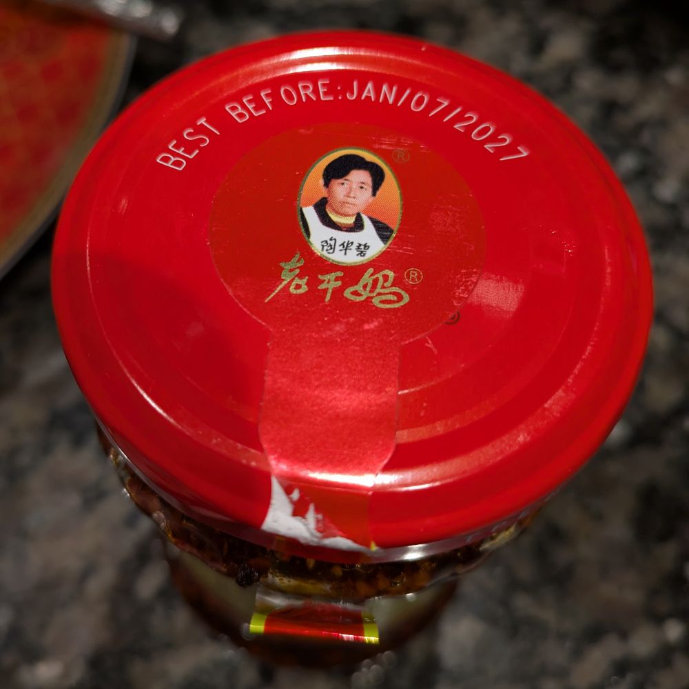 A jar of spicy chili crisp, mankind's crowning culinary achievement, with an expiration date of January 2027. This stuff isn't making it to December.