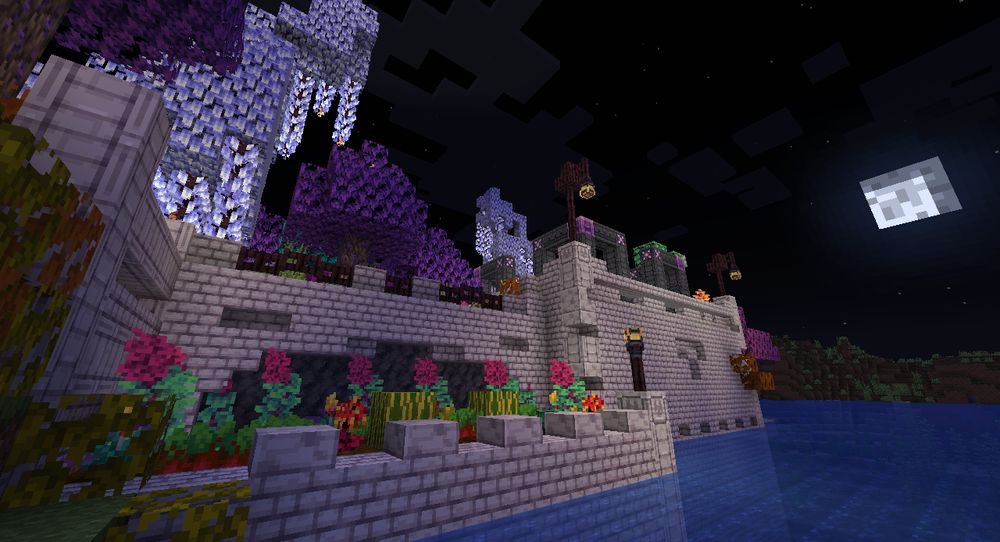 White brick castle with a pastel themed garden surrounded by trees at night time.