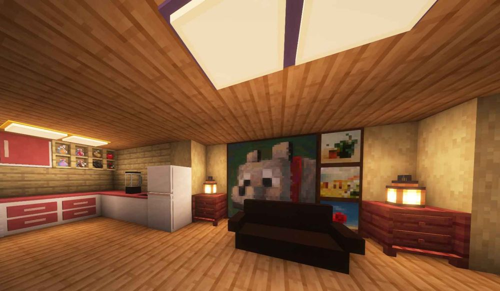 A view from inside a house, showing off new furniture from Skniro’s Furniture. There is a brown couch with nightstands behind and to its sides. There are also several paintings behind it. Additionally, there is a kitchen to the left with a fridge, countertops, a blender, and some cabinets.