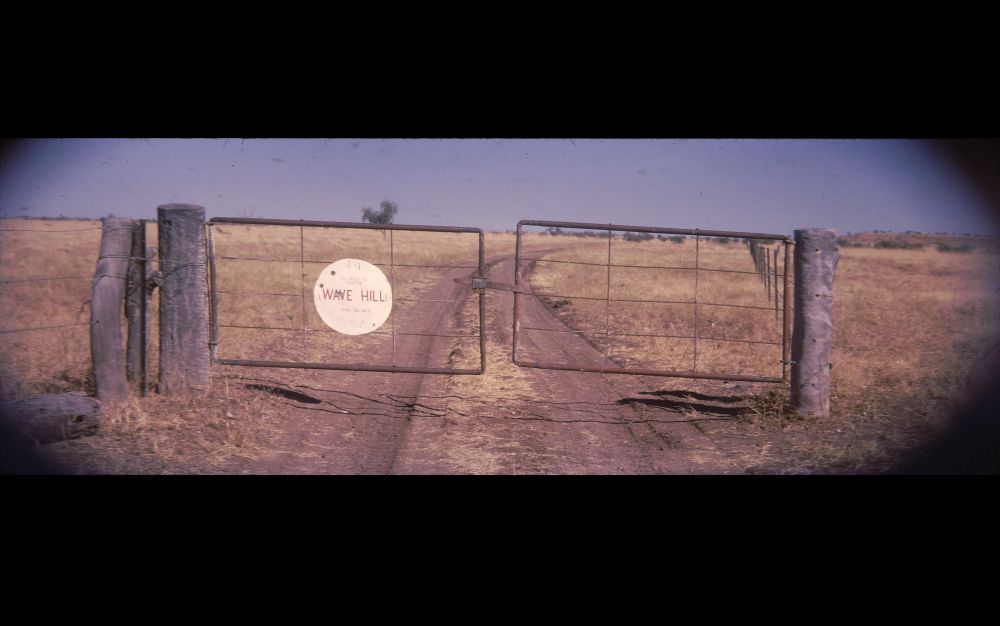 A widescreen view of a weather-worn gate across an unsealed road through northern Australian grassland. The left side of the gate bears a white roundel, indicating that it marks the entrance to the Wave Hill cattle station, twenty miles away. The photographer, a Commonwealth Government radio technician, was probably more concerned with the gate’s suitability for the CinemaScope frame ratio than the living and working conditions of the station’s Gurindji employees at the time but history remembers Wave Hill in the nineteen-sixties as the crucible of the Land Rights movement, celebrated in Kev Carmody and Paul Kelly’s song “From little things big things grow”