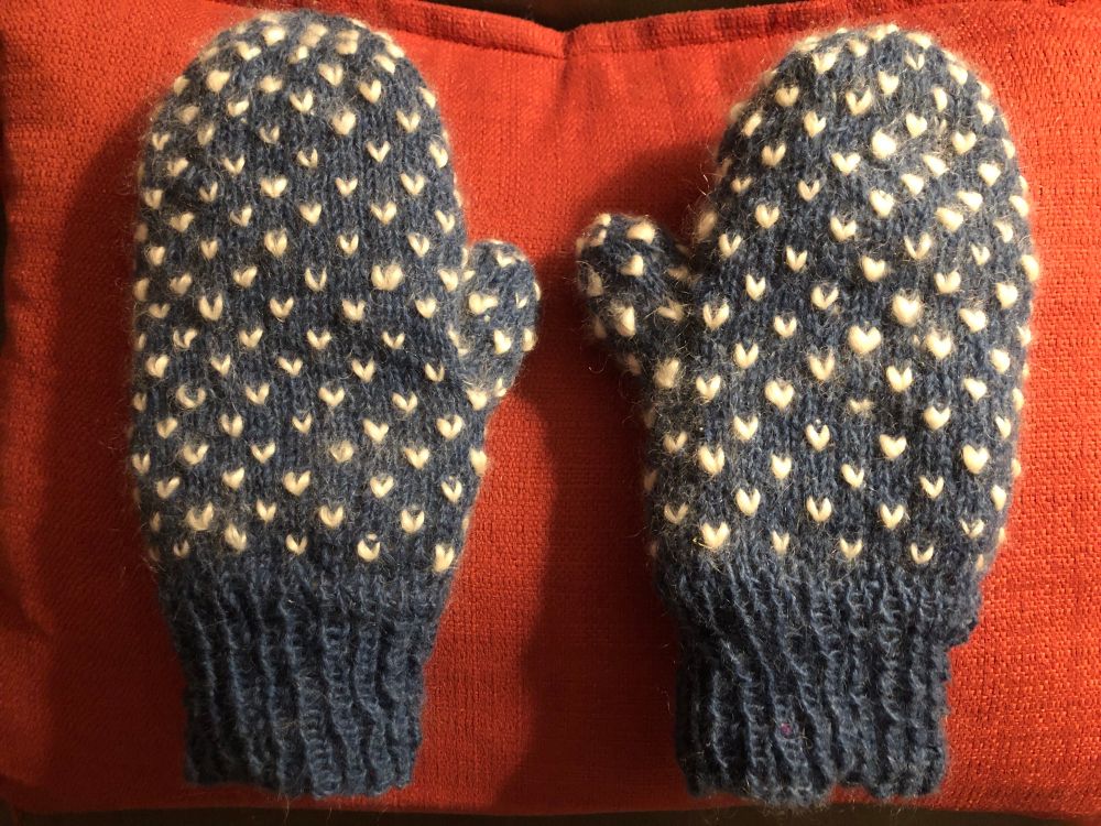 A pair of complete thrummed mittens hand knit in a rustic blue wool yarn with natural cream coloured roving thrums.