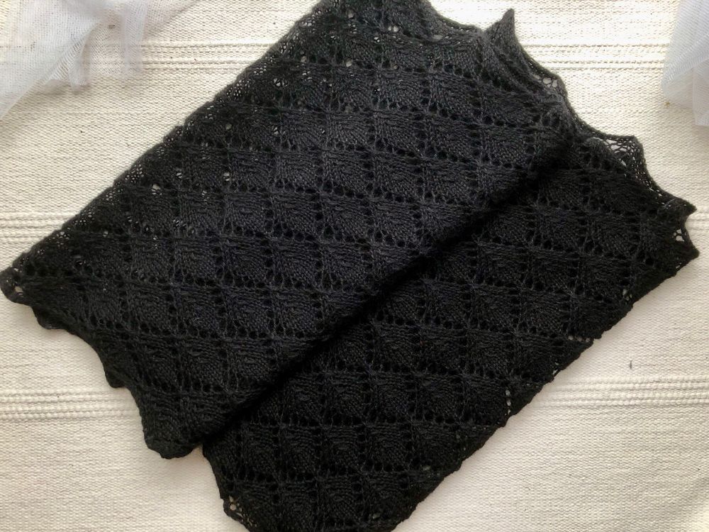 A folded black handknit lacework scarf with leaf lace motif. 