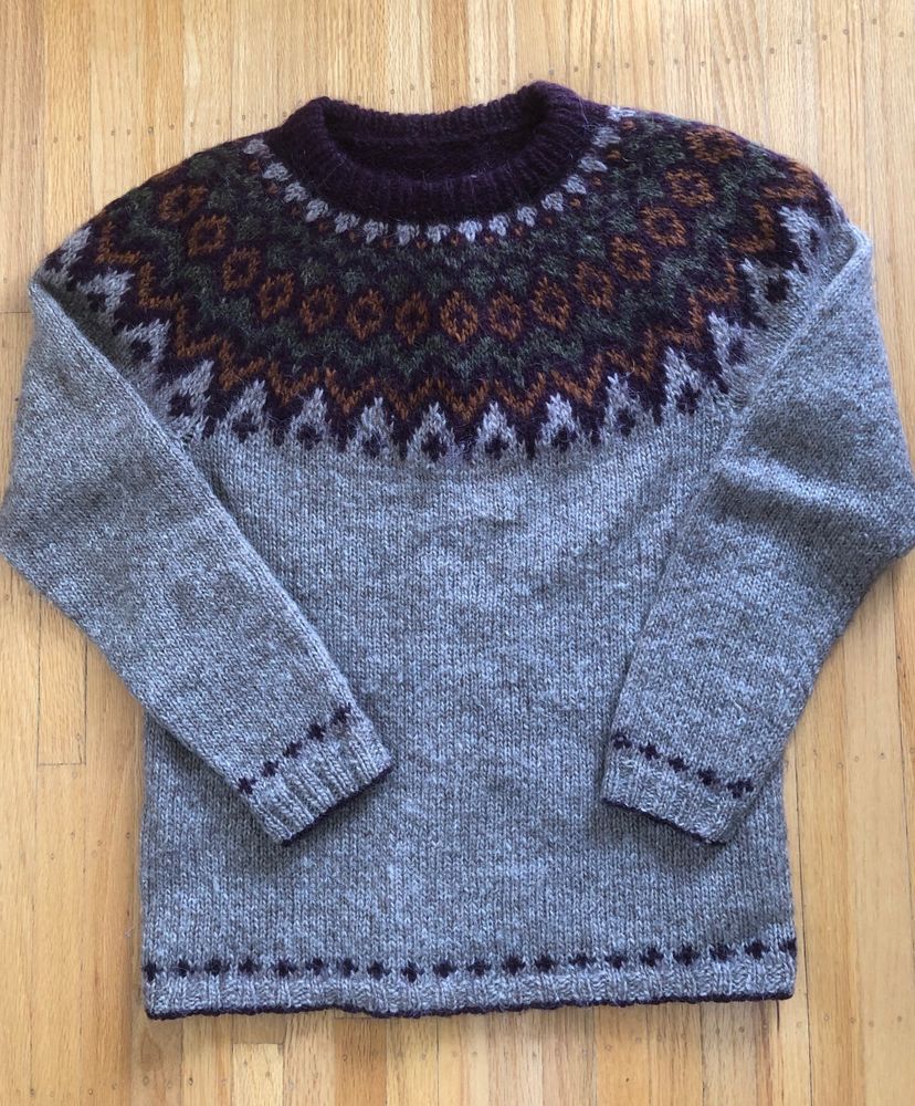 A flatlay photo of a riddari pullover sweater knit in earthy shades of istex lettlopi - mc is oatmeal, with cc of eggplant purple, rusty orange, forest green.