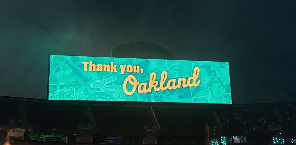 The Coliseum scoreboard glowing green in the night after the last A's fireworks show at the Coliseum. It says, "Thank you, Oakland."