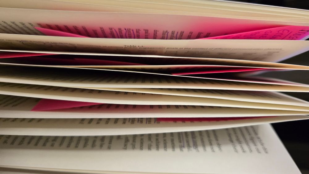 Paperback book viewed from side. Pages are fluffed open with the many pink sticky notes in between pages.