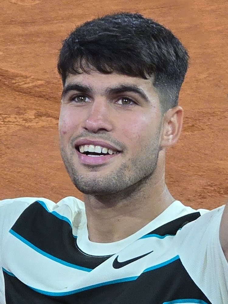A smiling Carlos Alcaraz with a lot of hair.