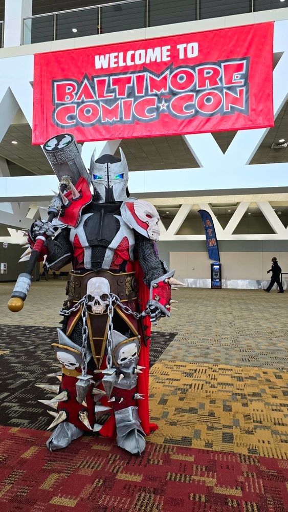 Medieval Spawn with hammer standing in front of banner that says "welcome to Baltimore Comic Con."