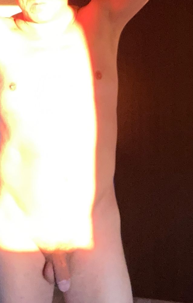 An unclothed man standing full frontal with bright sunlight partially illuminating his front. The hands are placed behind his head, but the face cannot be seen (outside of frame). #nonsexualnudity