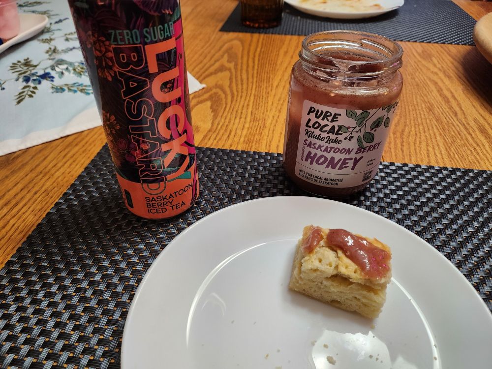 A small piece of bannock with pinkish Saskatoon berry honey on it and a can of Lucky Bastard Saskatoon Berry Iced Tea. Getting the whole Saskatoon experience one last time. 