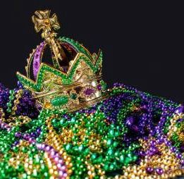 Photo of a Mardi Gras crown, lying on top of green, yellow, and purple Mardi Gras beads 