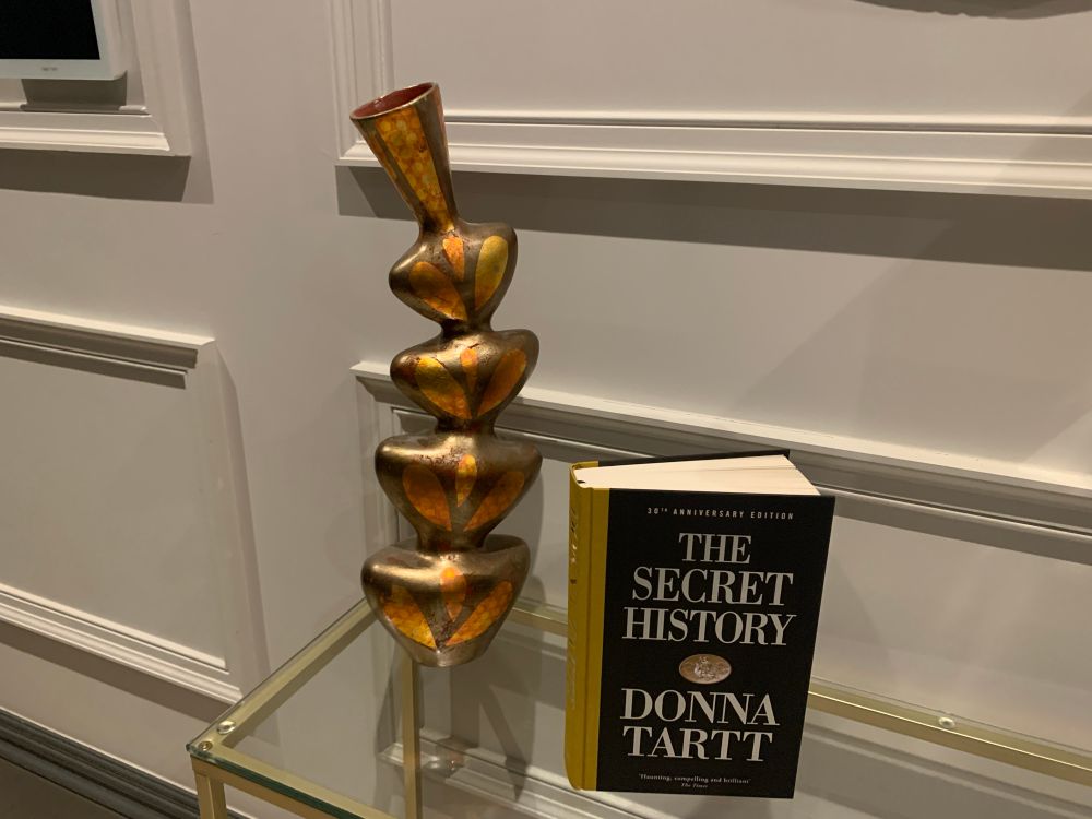 Picture of special edition of The Secret History on glass console table next to gold coloured glass ornamental vase. 