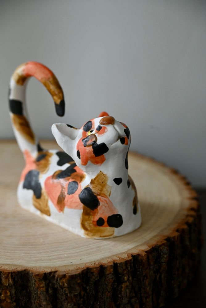 Ceramic cat figurine on a wood round, viewed from an angle.