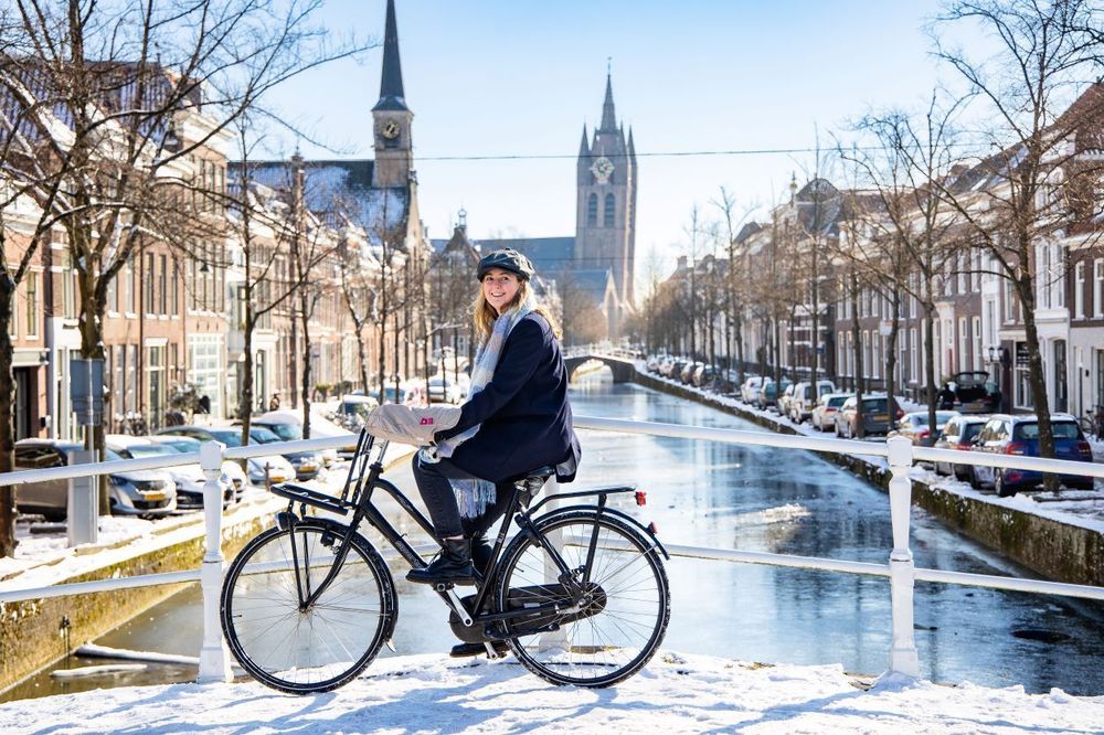 Woman riding a bike across a snowy bridge in Dutch old city