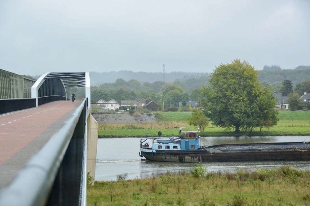 Cyclist on cycling bridge with boat going under