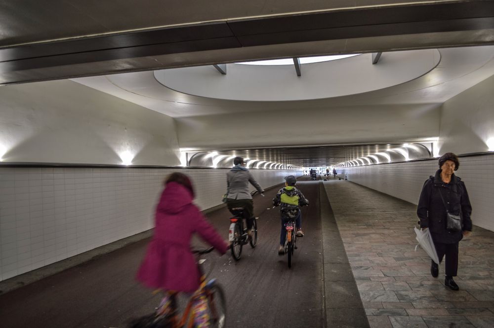 People cycling through a tunnel on a cycle path next to a footpath