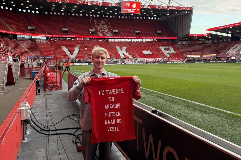 Fan holding a shirt inside the stadium that says, "FC Twente and Arcadis cycle to De Veste." (in Dutch)