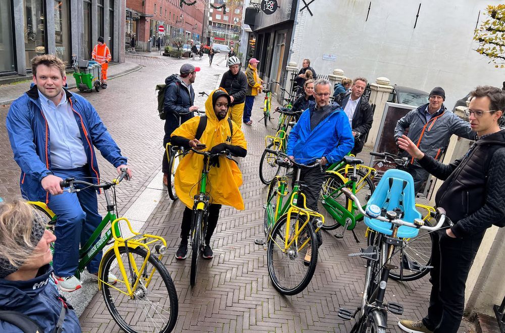 Group of people with bikes standing in the street with someone presenting to them

