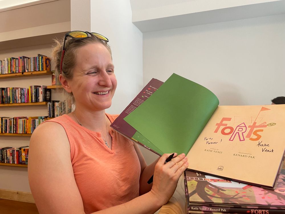 Katie Venit, the author of Forts, holding up a copy of the title page with an inscription that says “forts forever”