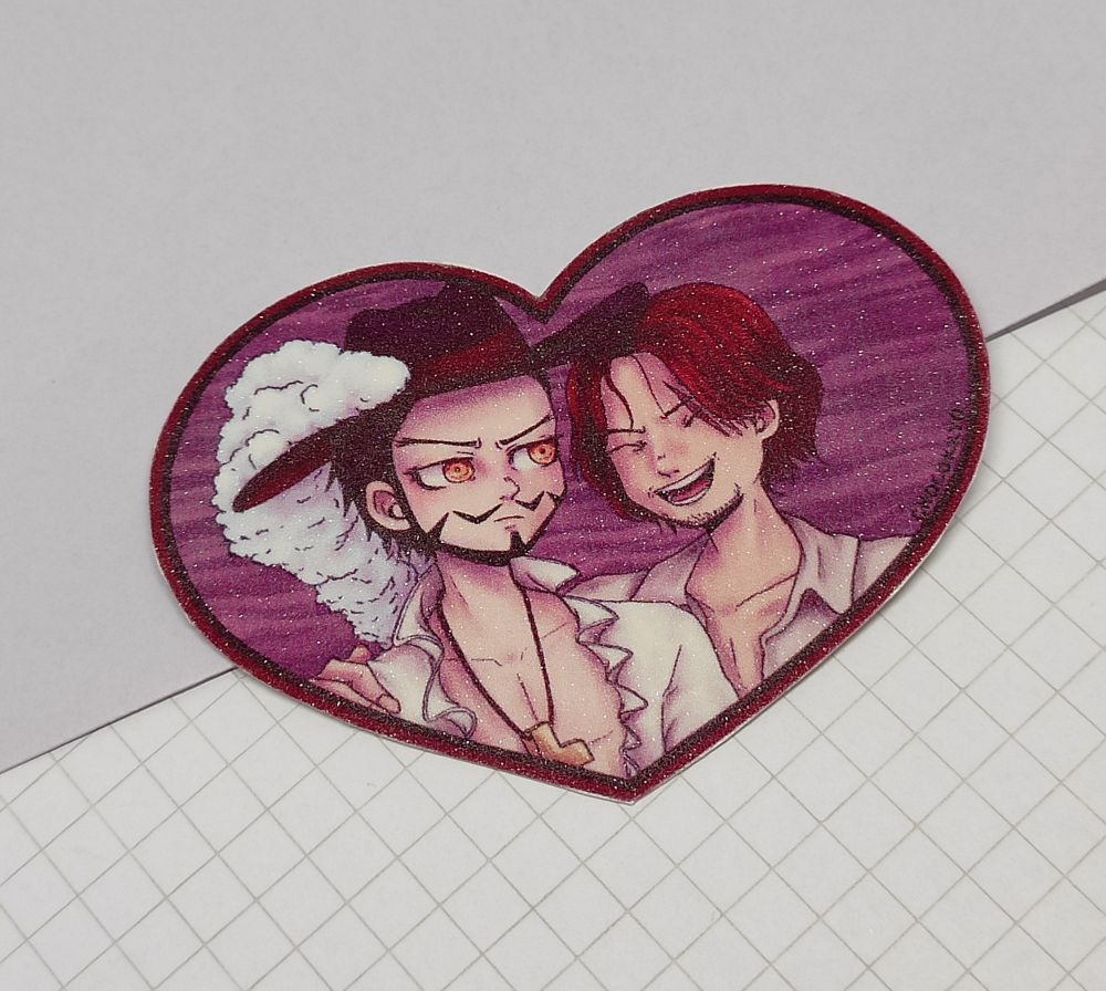 foto de um adesivo em formato de coração com os personagens mihawk e shanks de one piece. o adesivo tem efeito de glitter 