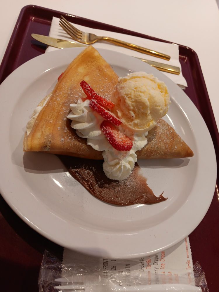 Folded crepe with strawberries, Nutella, whipped cream, ice cream, and powdered sugar on a white plate. 